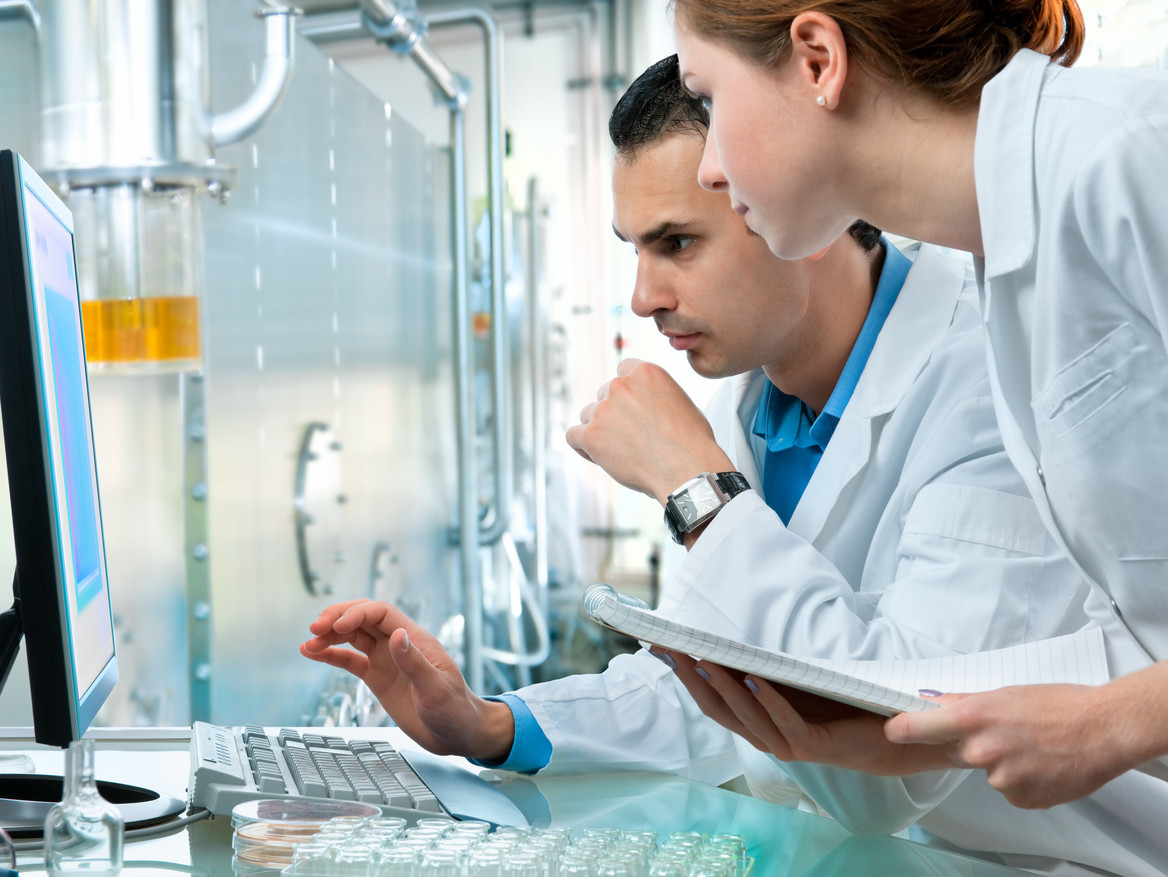 Two chemical industry workers look at a computer monitor.