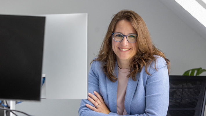 Eva Opitz sitzt am Schreibtisch und lächelt in die Kamera. Foto: Frank Eppler / IW Medien