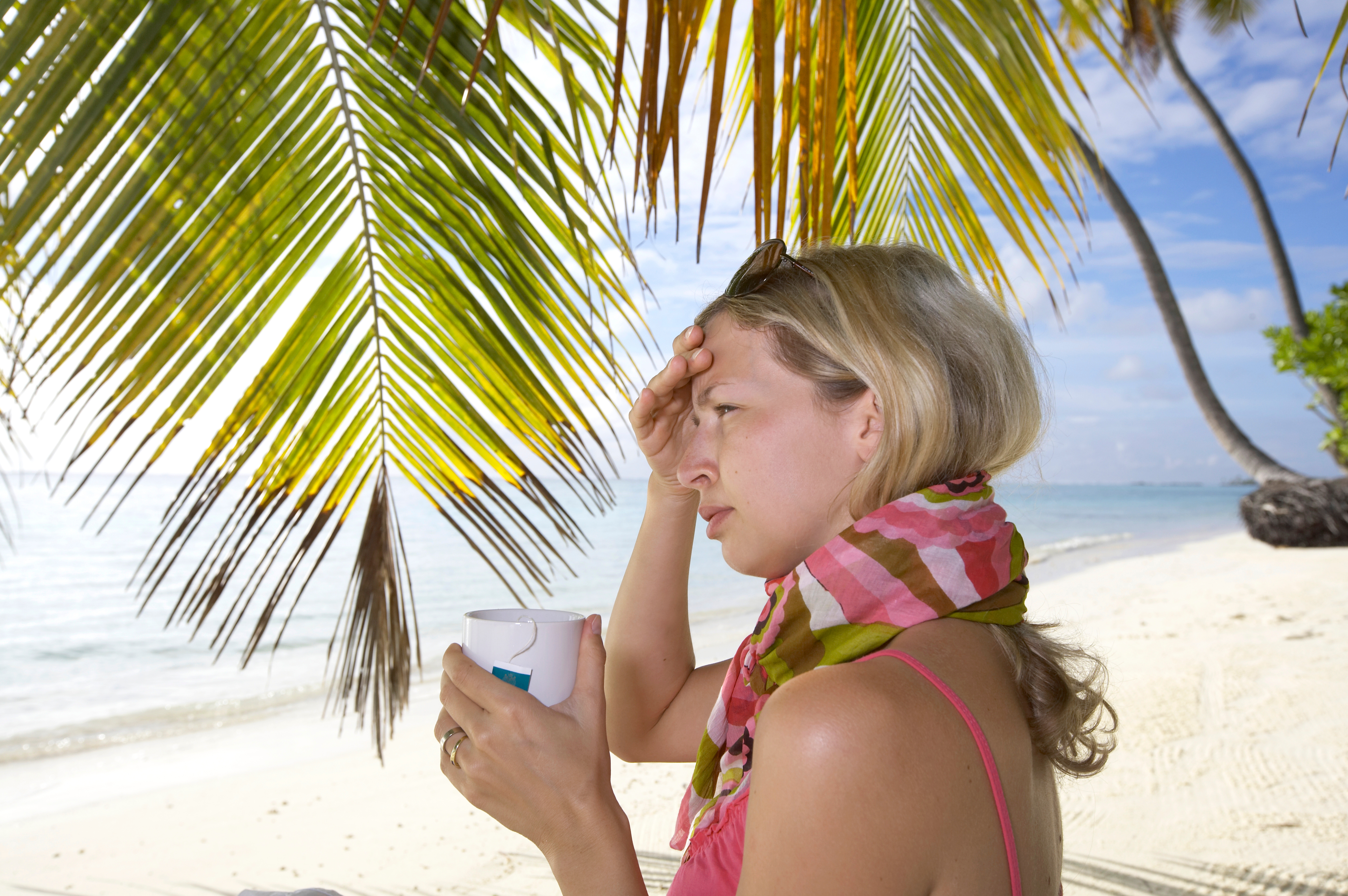 Eine Urlauberin am Strand mit Schal und einer Tasse Tee. 