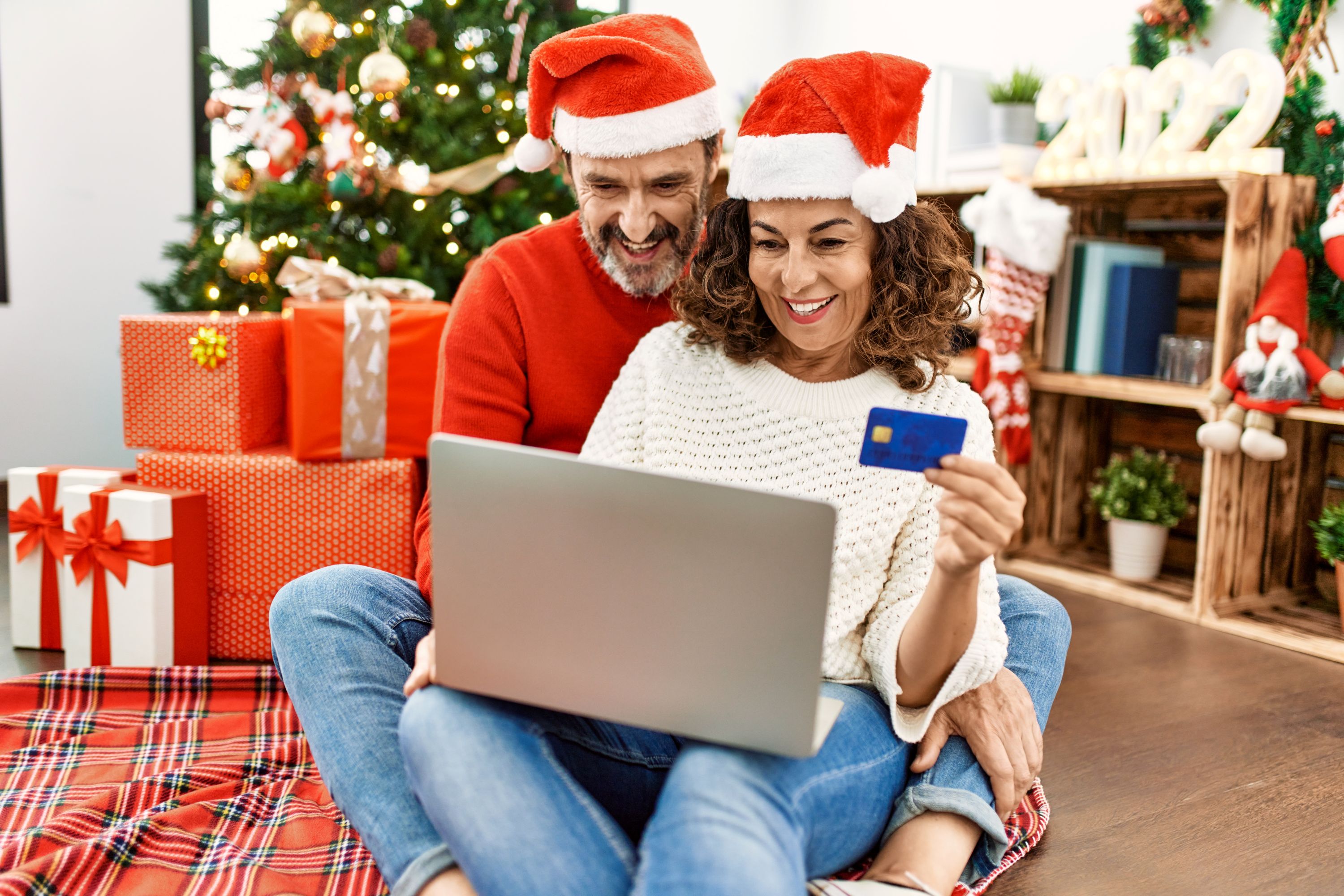 Ein Paar checkt erfreut den Kontostand unterm Weihnachtsbaum: Die Jahressonderzahlung ist eingetroffen.