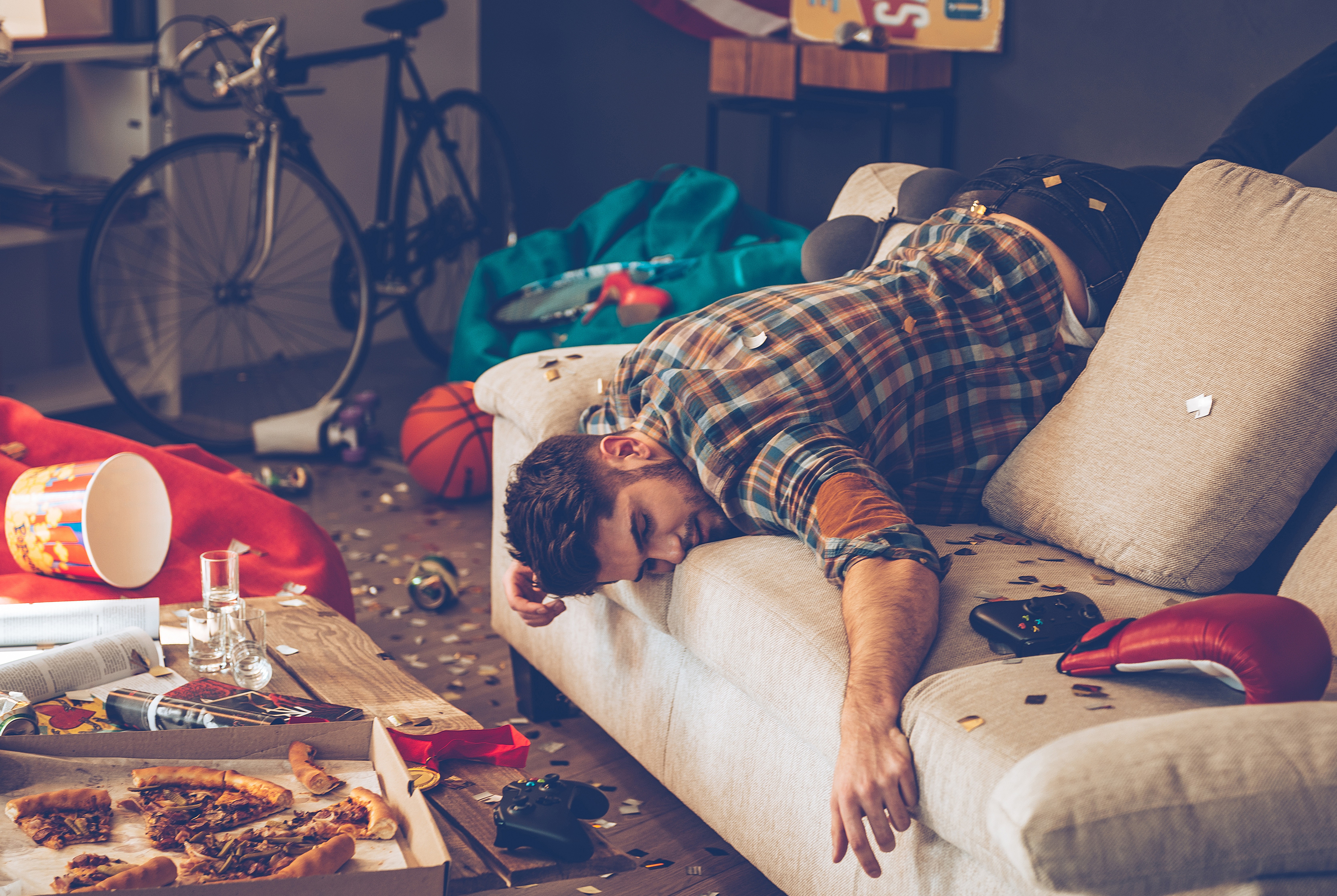 Junger Mann hängt nach einer Party kopfüber auf seinem Sofa.