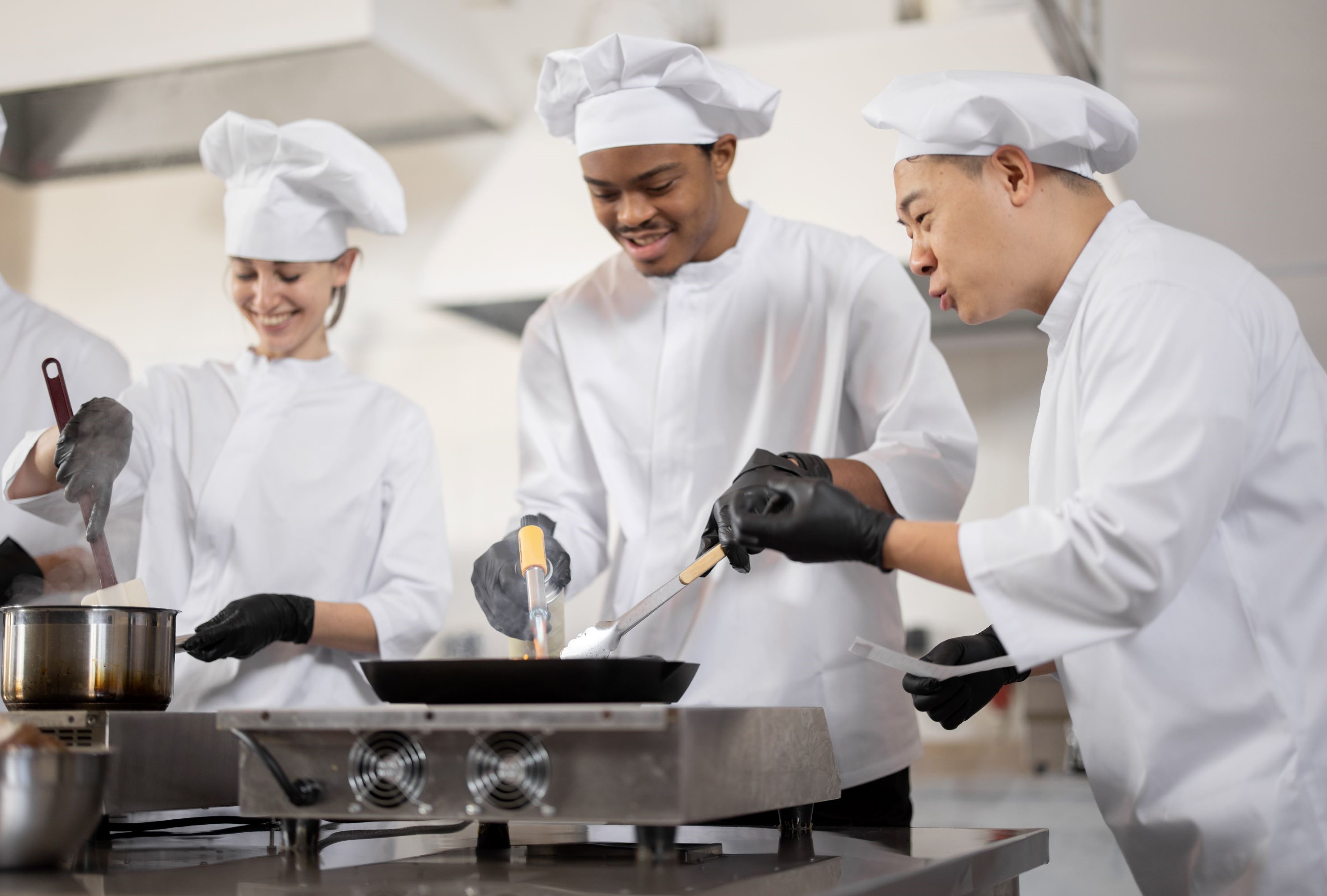 Multikulturelles Kochteam beim Kochen und Braten in einer professionellen Küche.